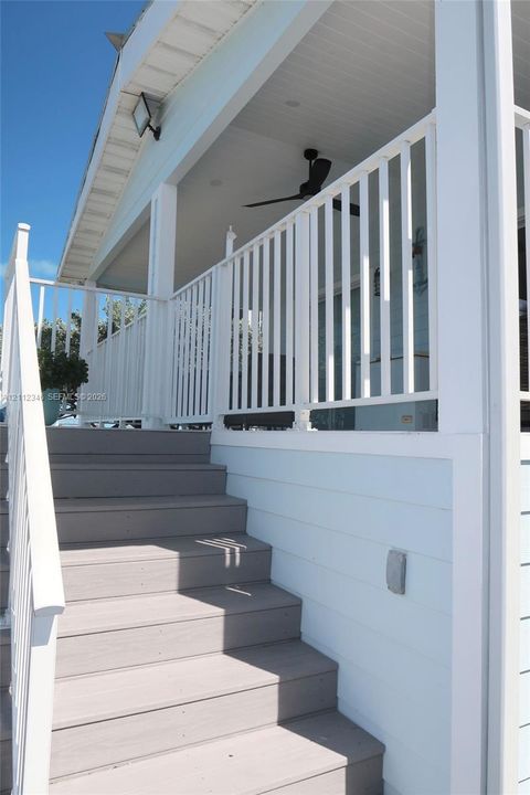 Covered porch featuring white vertical railing, a ceiling fan, light-colored horizontal siding, and staircase with composite-style decking