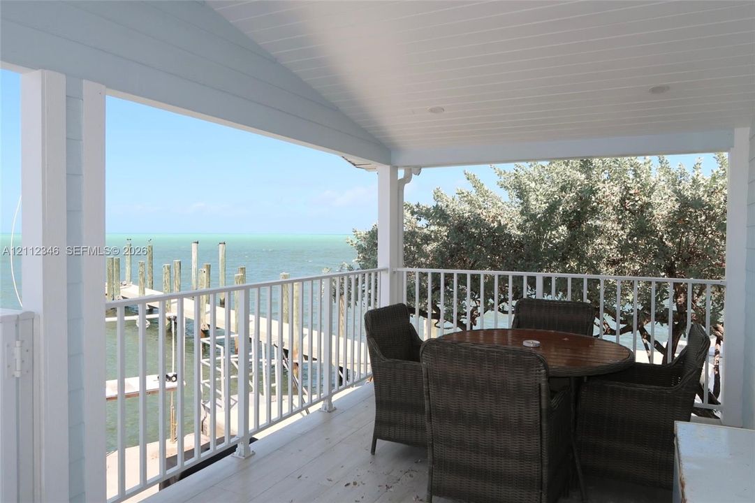 Covered balcony featuring beadboard ceiling, white metal railing, and direct water exposure with a private dock
