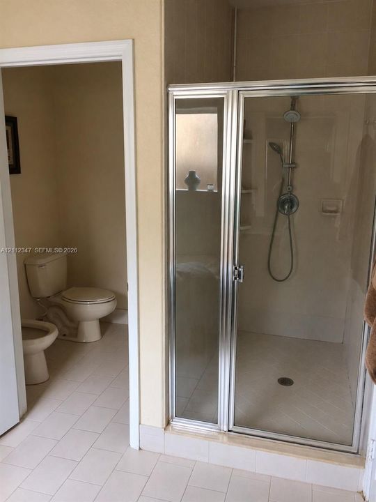 Bathroom featuring a glass-enclosed shower with a handheld showerhead, integrated shelving, and large-format tile flooring