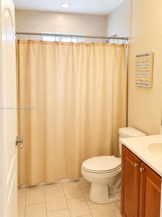 Bathroom featuring wood-finish cabinetry, a neutral-toned countertop with an integrated basin, ceramic tile flooring, and a recessed ceiling light