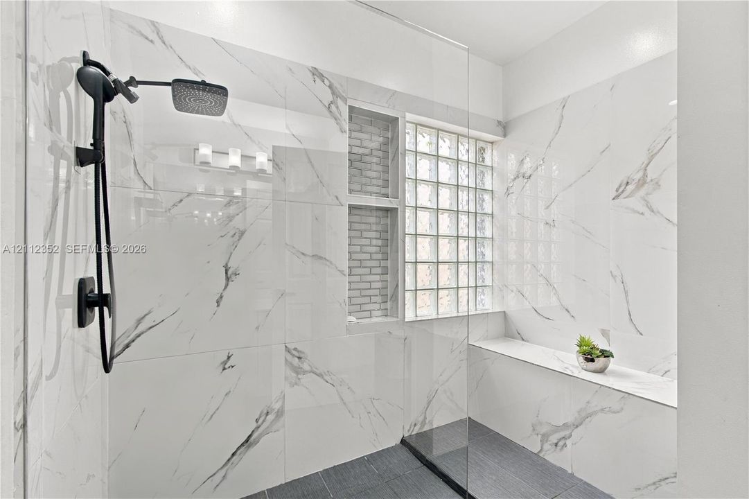 Walk-in shower featuring large-format stone-patterned wall tiles, dark floor tile, a glass partition, a built-in bench, and a matte black rainfall showerhead