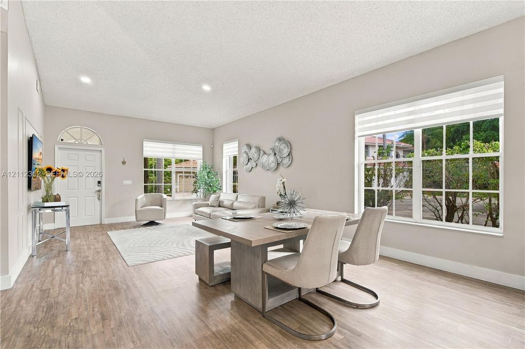 Open-concept living space featuring wood-finish flooring, recessed lighting, multiple oversized windows, and a front entry door with a transom window