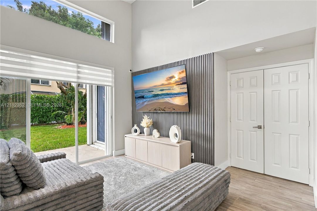 High-ceiling room featuring double-height windows, vertical slat wall paneling, sliding glass doors, and light-tone wood-finish flooring