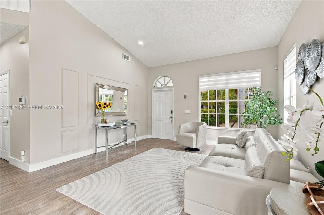 Living room featuring vaulted ceilings, wood-finish flooring, wall molding detail, and a front entry door with a transom window