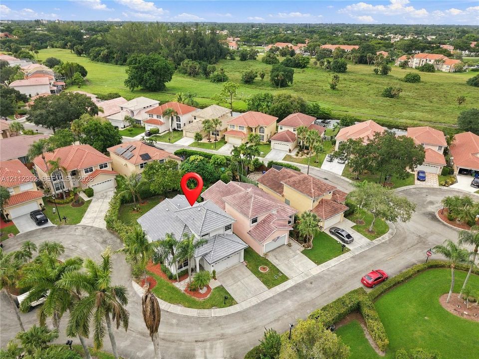 Aerial perspective featuring a tile roof, multi-level architectural design, attached garage, and paved driveway situated within a suburban landscape
