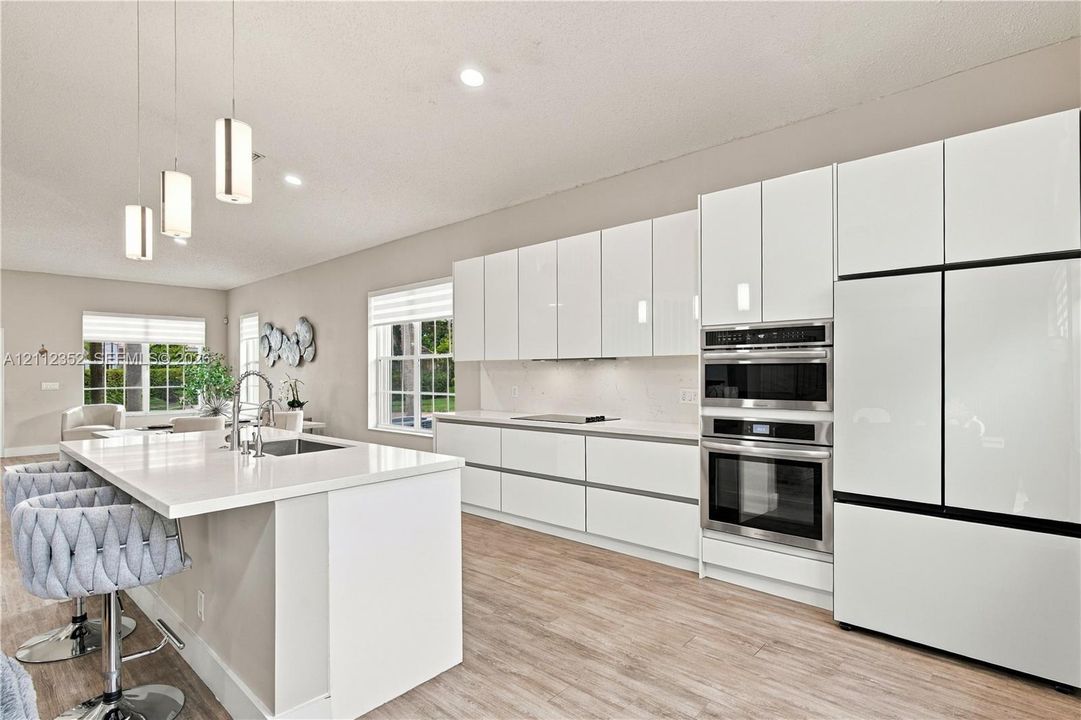 Kitchen featuring high-gloss white cabinetry, white stone-surface countertops, wood-finish flooring, built-in stainless steel appliances, and three glass pendant lights