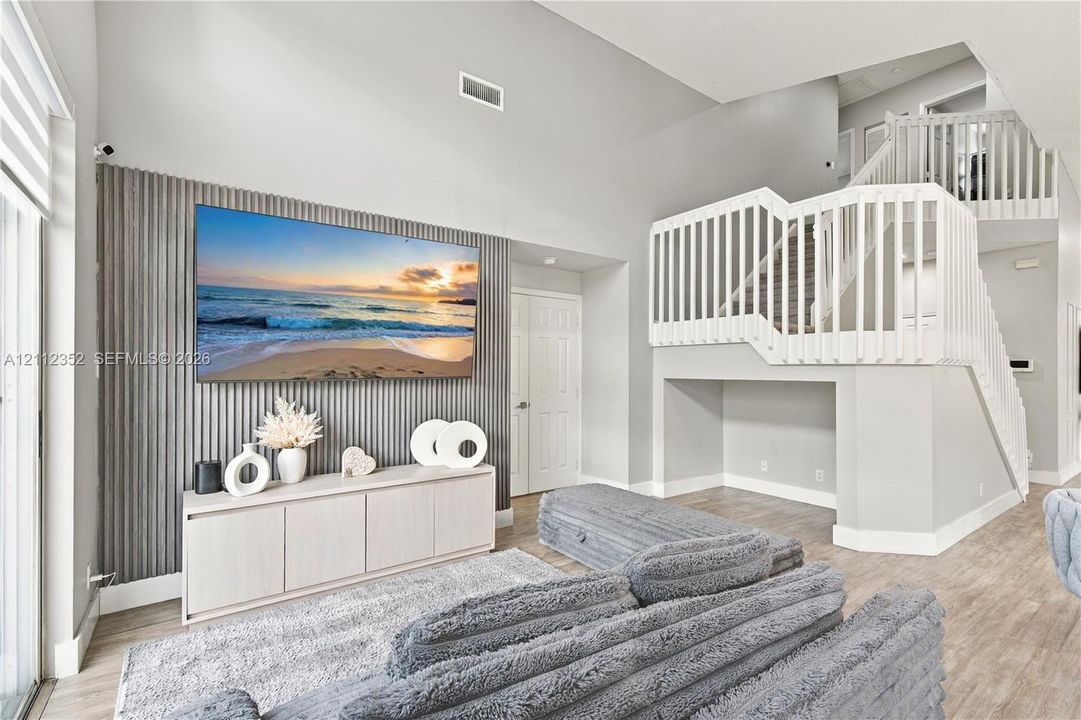 High-ceiling living area featuring a ribbed accent wall, wood-finish flooring, and a staircase with white vertical balusters
