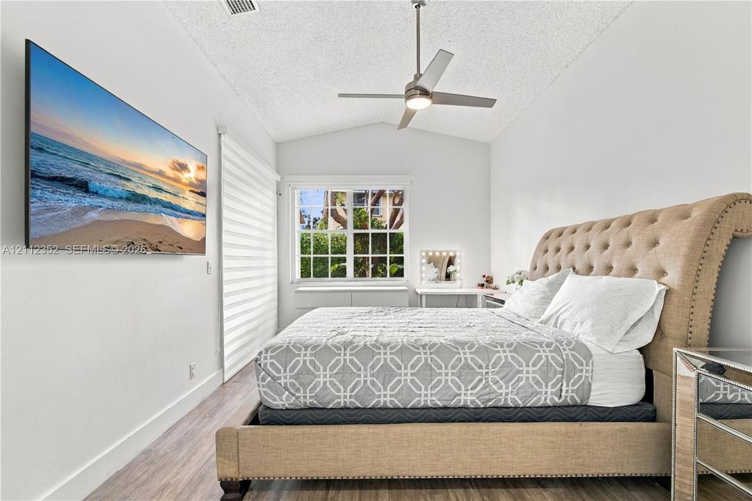 Vaulted ceiling featuring a central brushed-metal ceiling fan, wood-finish flooring, and a multi-pane window