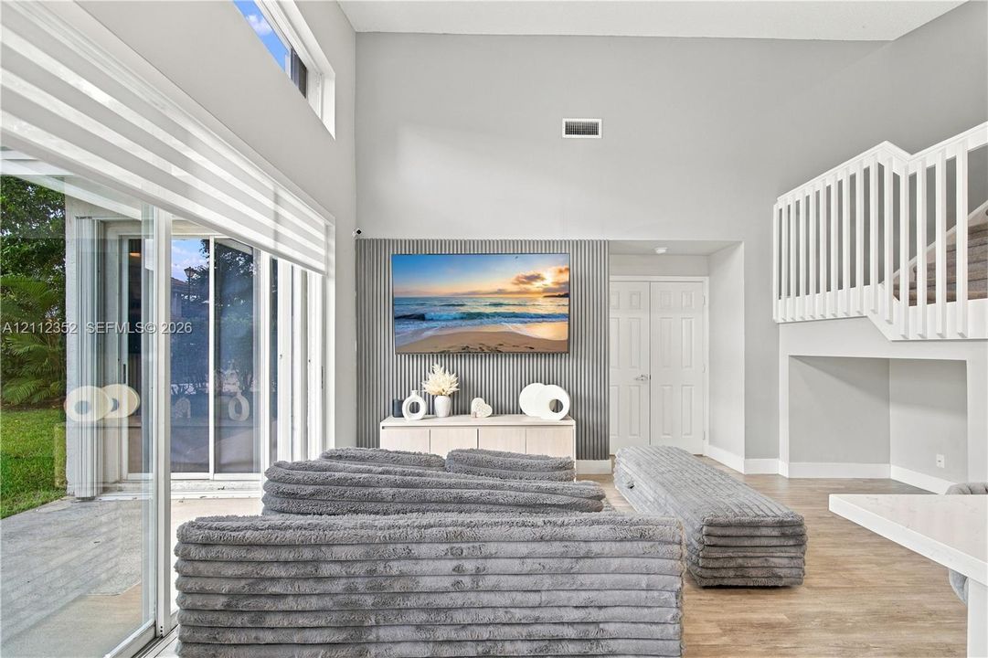 Vaulted ceilings featuring expansive sliding glass doors, a ribbed accent wall, wood-finish flooring, and a mezzanine staircase with white balusters