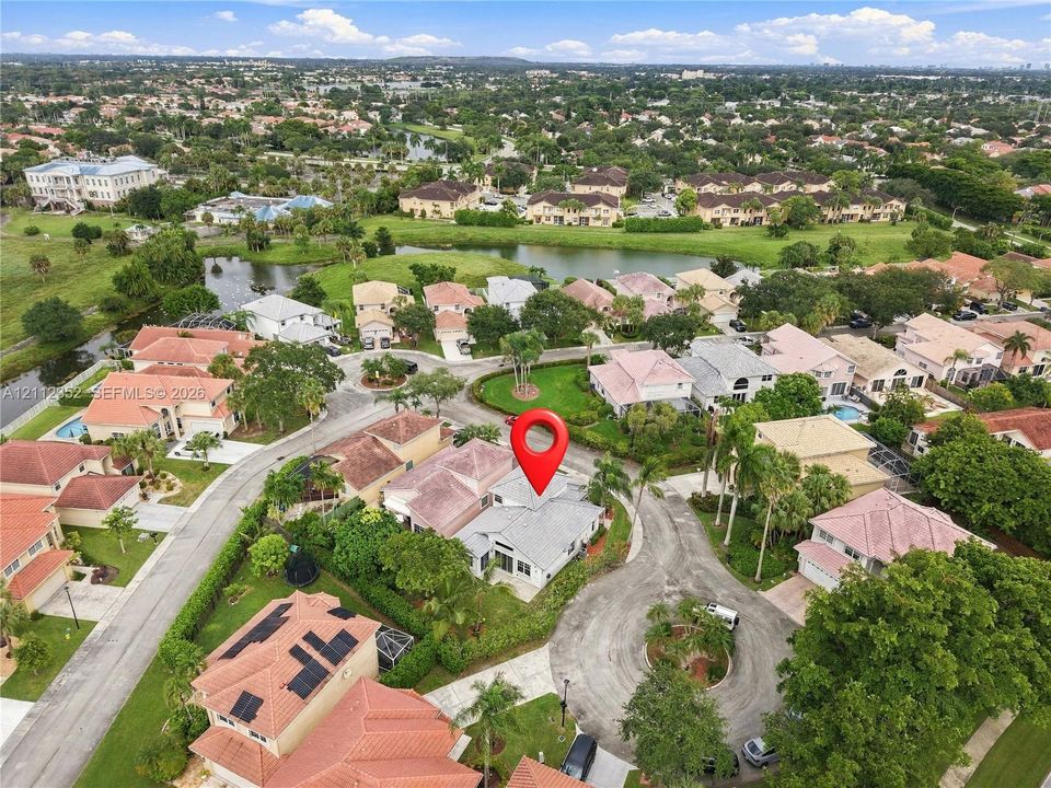 Aerial perspective of a single-story residence situated within a cul-de-sac, featuring a shingle roof, paved driveway, and mature landscaping