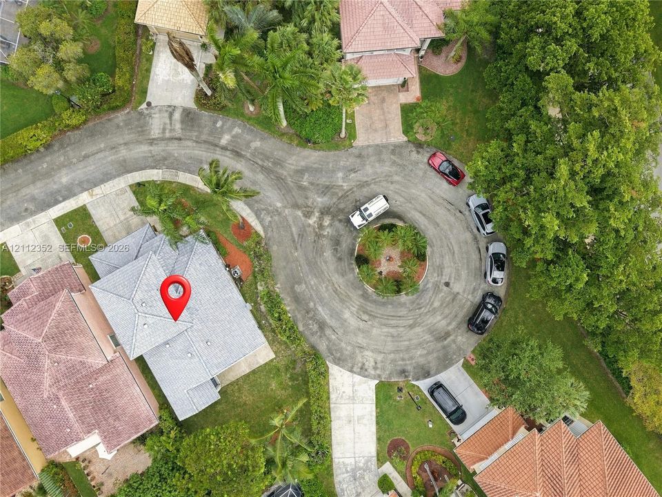 Aerial view of a residential property situated on a cul-de-sac, featuring a shingled roof, concrete driveway, and landscaped surroundings