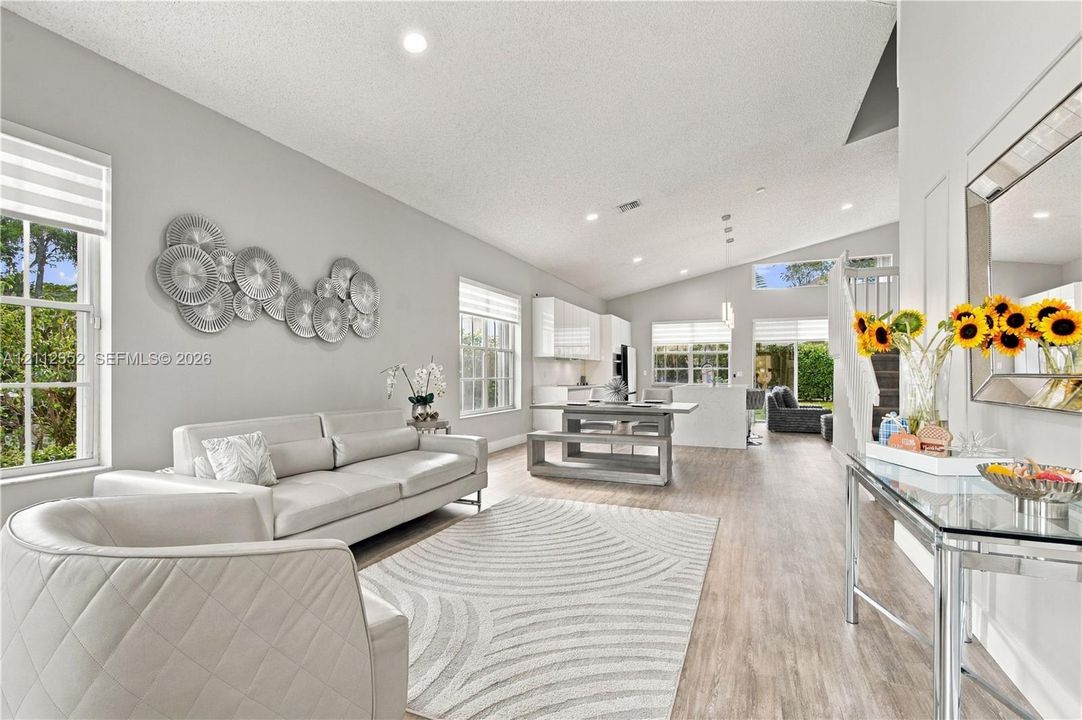 Open-concept interior featuring vaulted ceilings, wood-finish flooring, recessed lighting, and multiple windows with integrated blinds
