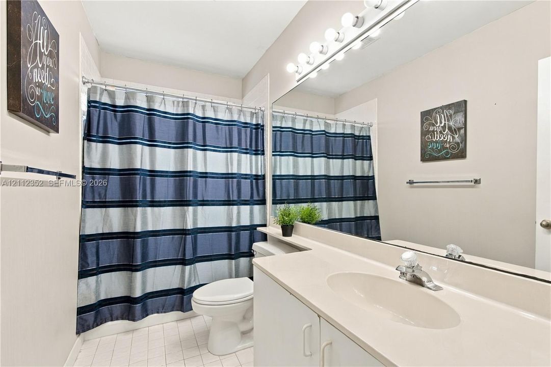 Bathroom featuring a vanity with integrated sink, expansive wall-to-wall mirror, multi-bulb vanity lighting, and tile flooring