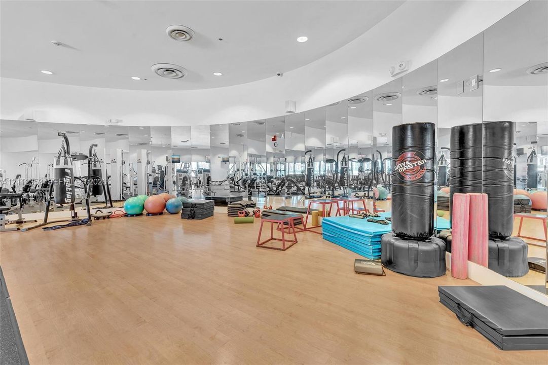 Fitness space featuring wood-finish flooring, full-wall mirrors, recessed lighting, and integrated ceiling ventilation