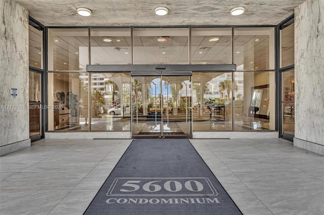 Building entrance featuring a stone-clad facade, expansive floor-to-ceiling glass paneling, automatic sliding doors, and recessed ceiling lighting