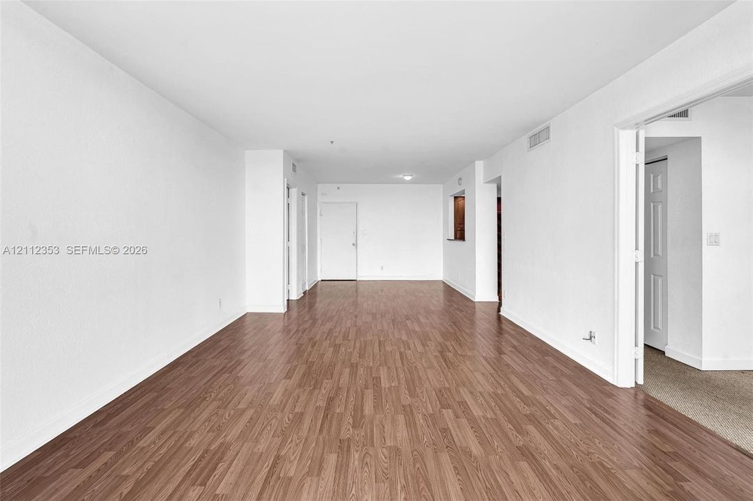 Open-concept interior featuring wood-finish flooring, neutral white walls, and a pass-through window