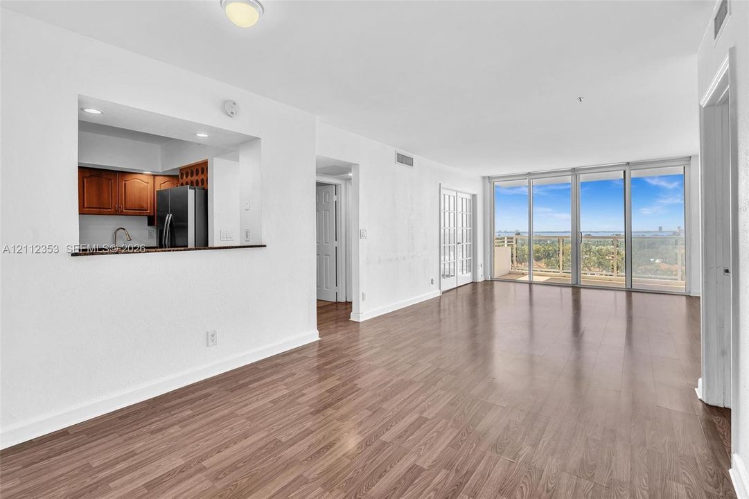 Open-concept interior featuring wood-finish flooring, a pass-through kitchen window, dual-pane floor-to-ceiling glass sliding doors, and an exterior balcony