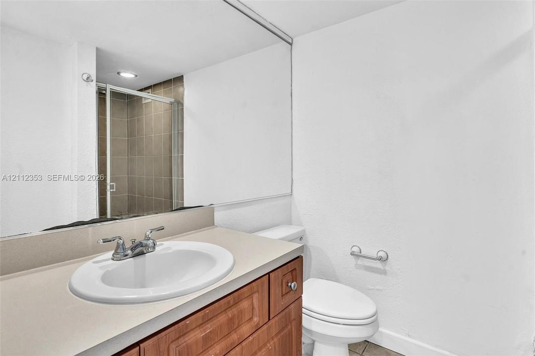 Bathroom featuring a wood-finish vanity with a stone-composite countertop, integrated sink, full-width mirror, and a glass-enclosed shower with tile surround