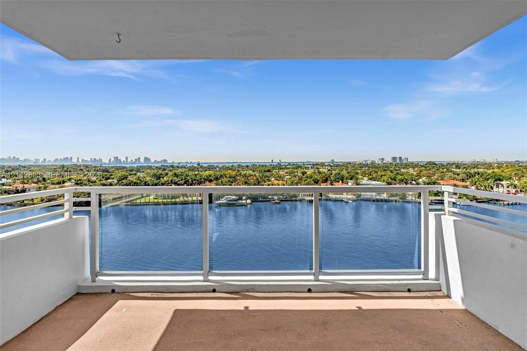 Private balcony featuring glass panel railings, solid white metal framing, and a concrete floor surface with a water-facing orientation