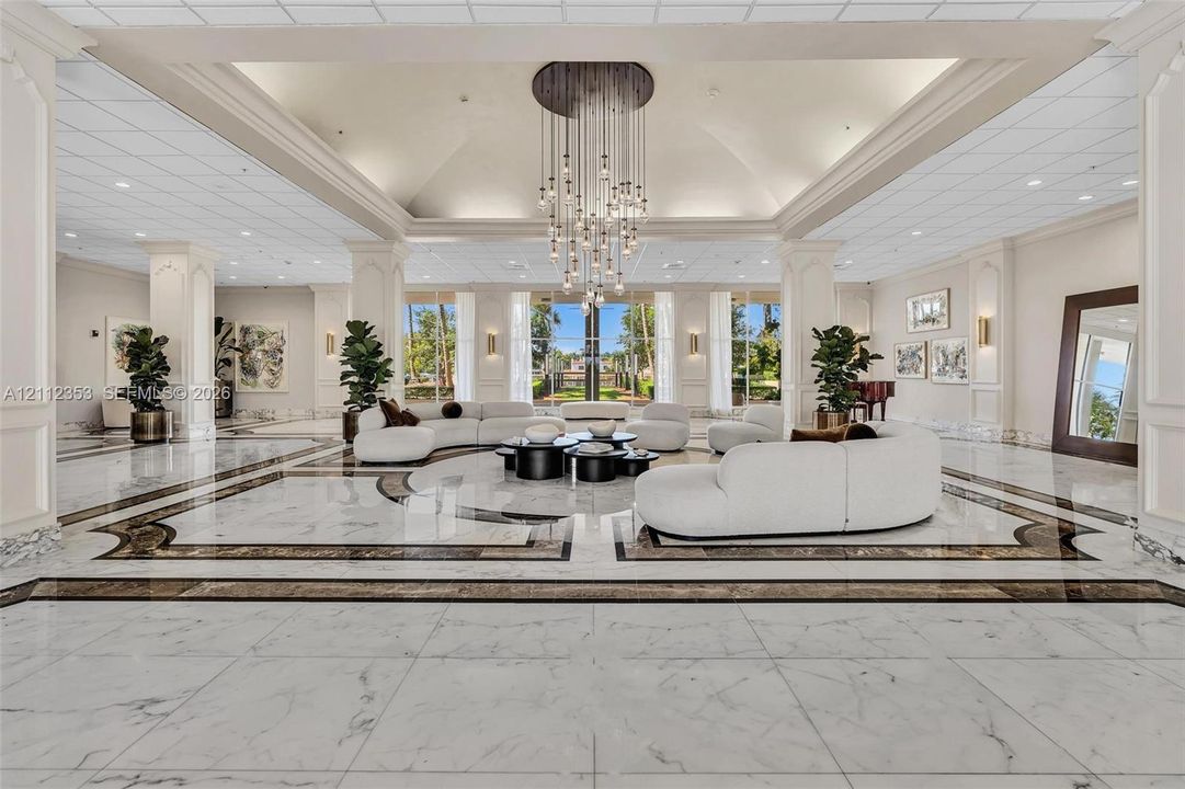 Grand foyer featuring high tray ceilings, polished stone flooring with decorative inlay, a multi-tiered crystal chandelier, and floor-to-ceiling windows