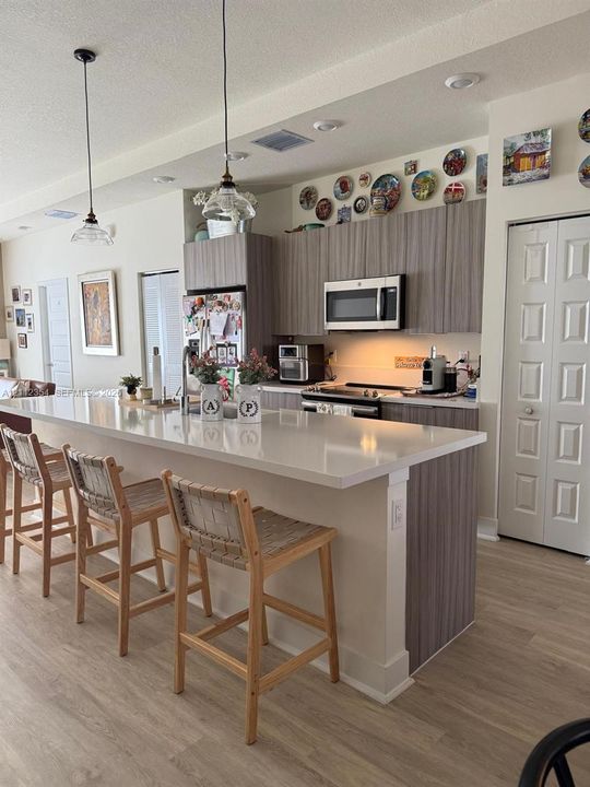Kitchen featuring an expansive island with a light-toned solid surface countertop, wood-finish cabinetry, built-in microwave, recessed lighting, and pendant fixtures