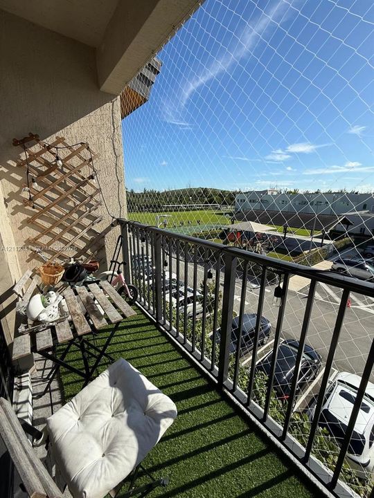 Covered balcony featuring synthetic turf flooring, black metal railing, and protective mesh screening