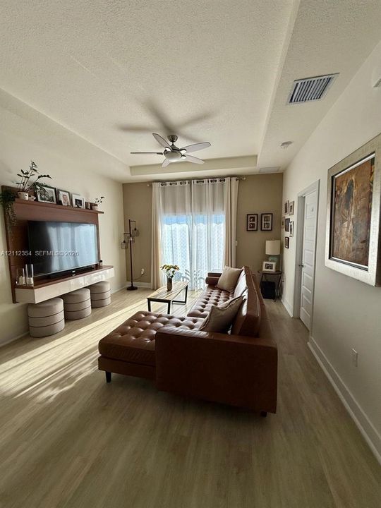 Tray ceiling with a central multi-blade ceiling fan, wood-finish flooring, and a wall-mounted built-in media console with integrated shelving
