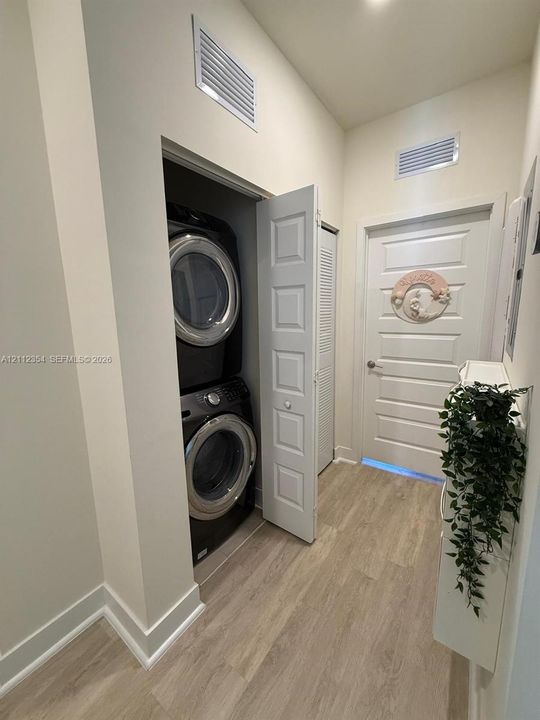 Laundry area featuring wood-finish flooring, a stacked appliance unit, and a five-panel interior door