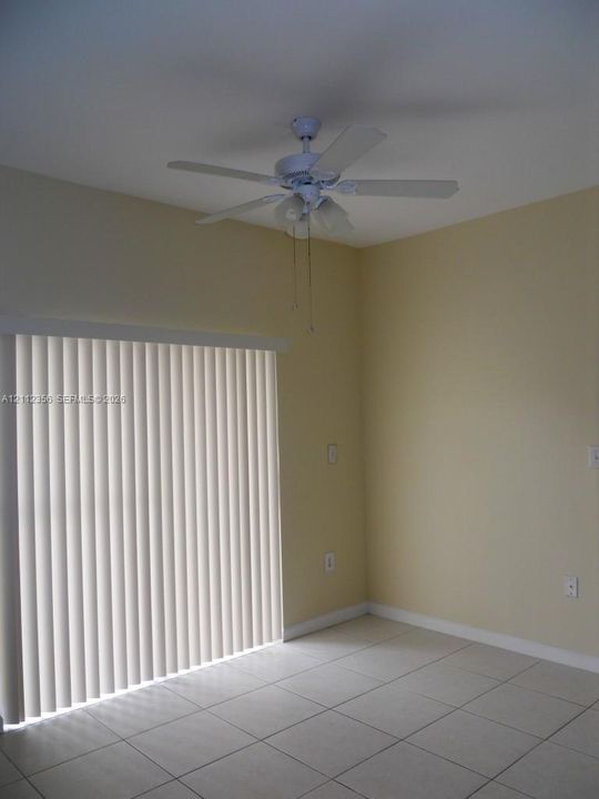 Room featuring ceramic tile flooring, a multi-blade ceiling fan with integrated lighting, and a vertical sliding glass door with blinds
