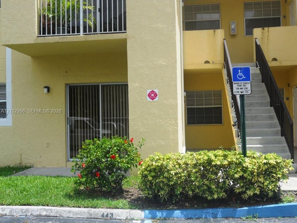 Multi-story exterior featuring stucco siding, sliding glass patio doors, a second-level balcony with metal railings, and concrete stairwell access