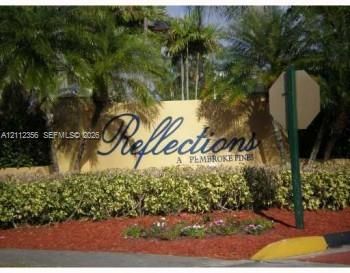 Reflections at Pembroke Pines monument signage featuring stucco wall construction, ornamental palm trees, and manicured shrubbery