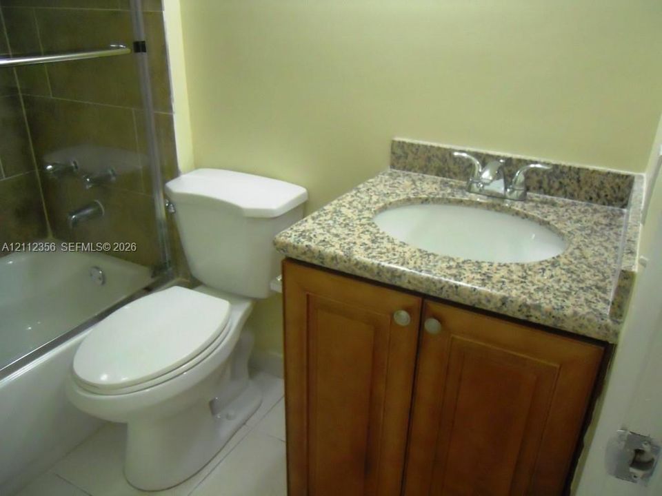 Bathroom featuring a wood-finish vanity with a stone-composite countertop, undermount sink, chrome faucet, and a shower-tub combination with tile surround