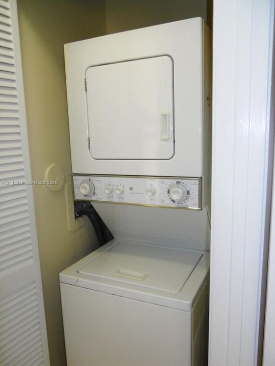 Stacked laundry unit with top-loading washer, front-loading dryer, and white louvered closet door