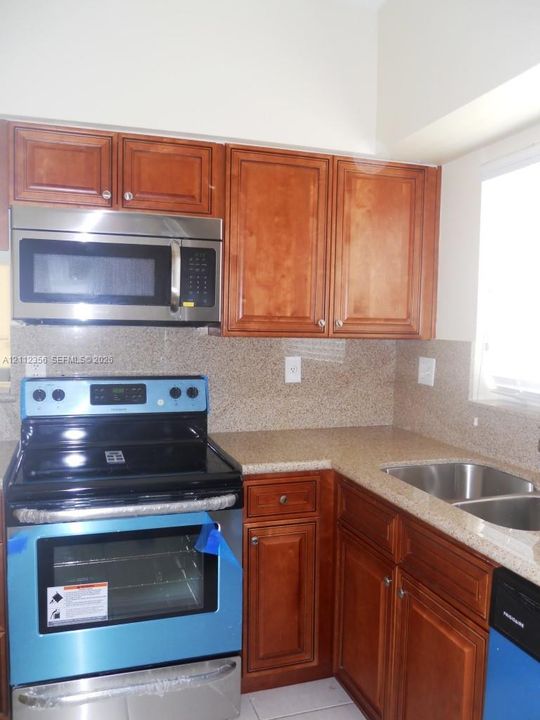 Kitchen featuring recessed-panel wood cabinetry, stone-finish countertops, full-height backsplash, stainless steel built-in microwave, and dual-basin under-mount sink
