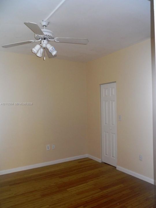 Room featuring wood-finish flooring, a white ceiling fan with integrated light fixture, and a white bi-fold closet door
