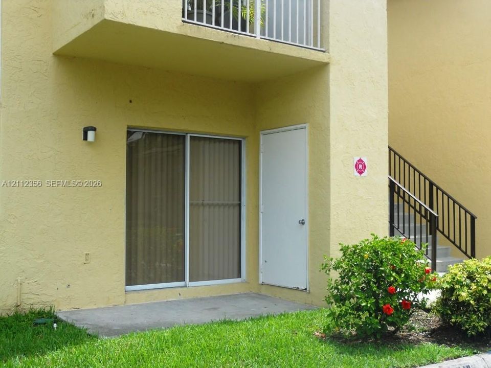 Stucco exterior featuring a concrete patio, sliding glass door, private exterior storage closet, and second-story balcony with metal railing