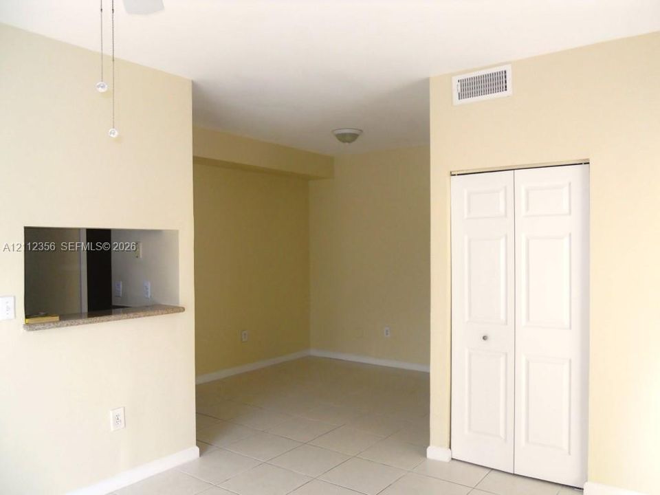 Neutral-toned interior space featuring light-colored tile flooring, a built-in pass-through opening with a stone-finish countertop, and a white bi-fold closet door