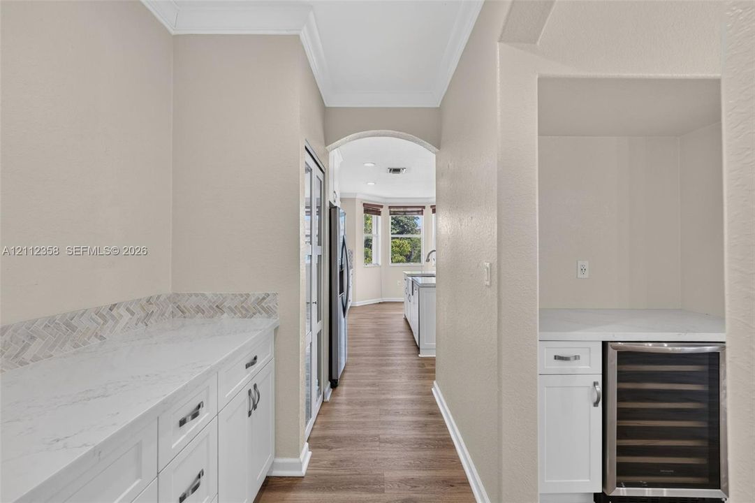 Butler pantry featuring white cabinetry, light-toned stone-finish countertops, a herringbone-patterned tile backsplash, and a built-in stainless steel beverage refrigerator