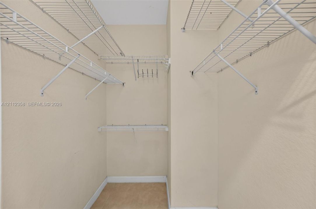 Walk-in storage space featuring multi-level white wire shelving and a mounted hook rack