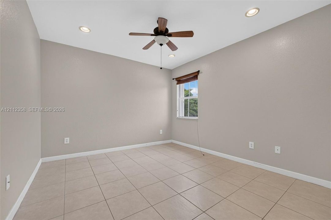 Neutral-toned room featuring large-format tile flooring, recessed lighting, a ceiling fan, and a single window with a wooden valance