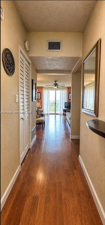 Hallway featuring wood-finish flooring, louvered bi-fold closet doors, and a built-in wall-mounted shelf