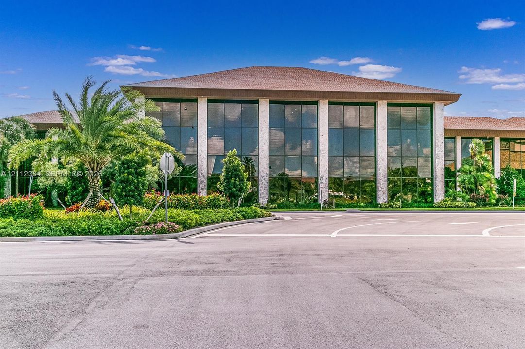 Commercial building exterior featuring extensive glass wall panels, structured stone columns, and a hipped roofline, surrounded by manicured landscaping