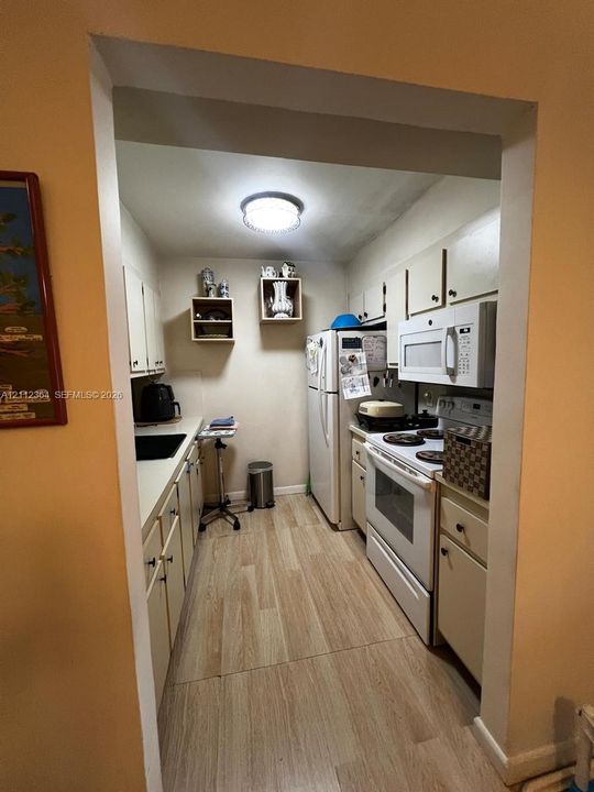 Kitchen featuring wood-finish flooring, white cabinetry, light-colored countertops, a built-in over-the-range microwave, and wall-mounted shelving