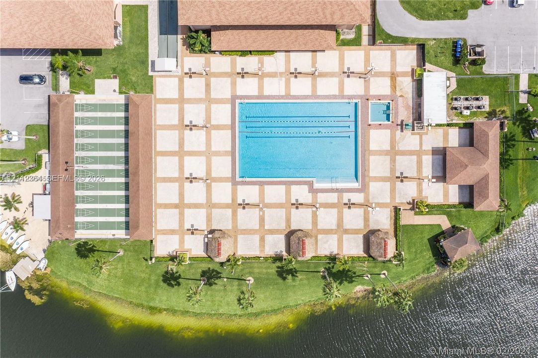 Community amenities including a swimming pool with lane markers, a designated spa area, shuffleboard courts, and surrounding landscaped grounds situated along a water feature