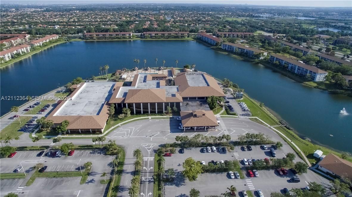 Aerial perspective featuring a multi-wing complex with shingled rooflines, extensive paved parking areas, and waterfront positioning