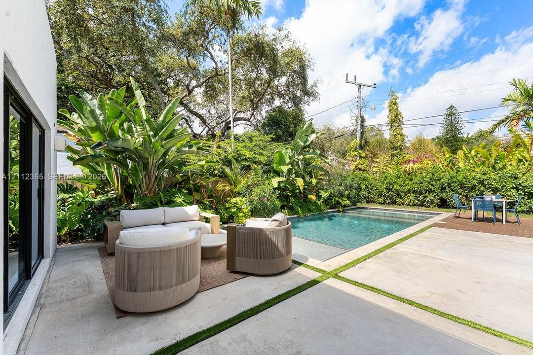 Outdoor space featuring an in-ground swimming pool, concrete patio with integrated artificial turf, and extensive perimeter foliage