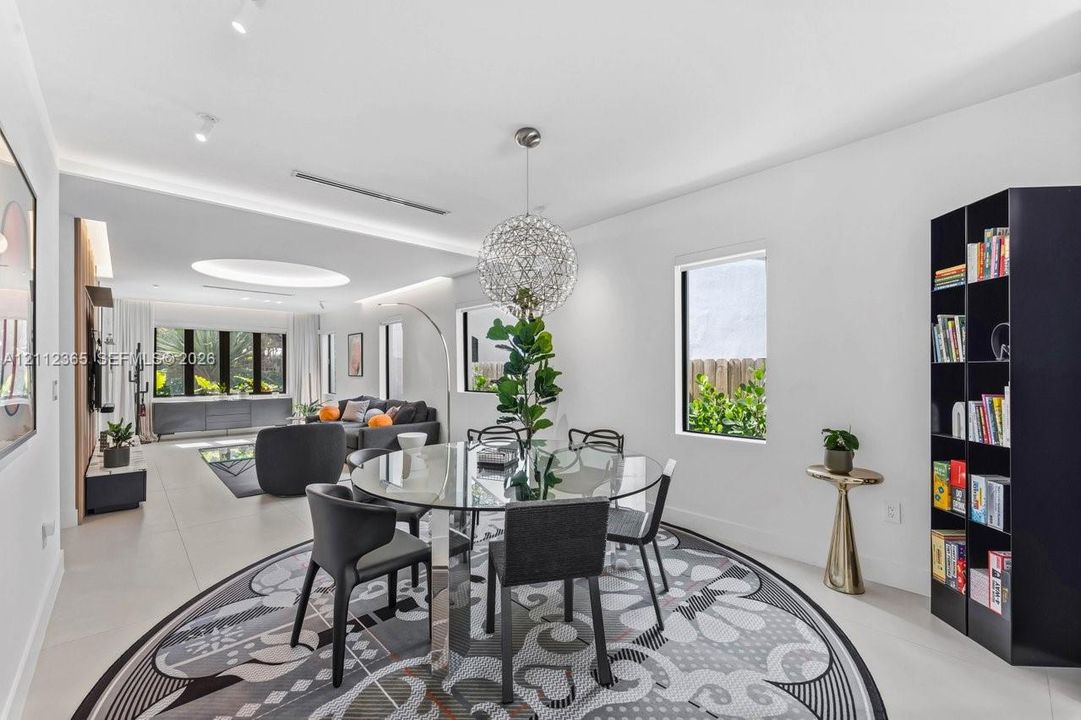 Open-concept living space featuring large-format tile flooring, a custom recessed ceiling with integrated lighting, a spherical statement chandelier, and multiple expansive windows