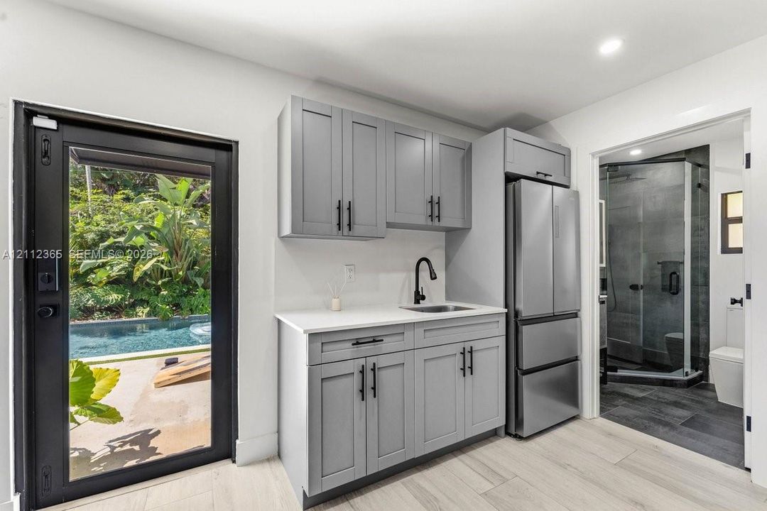 Kitchenette featuring grey shaker-style cabinetry, matte black hardware, solid surface countertops, and stainless steel refrigerator