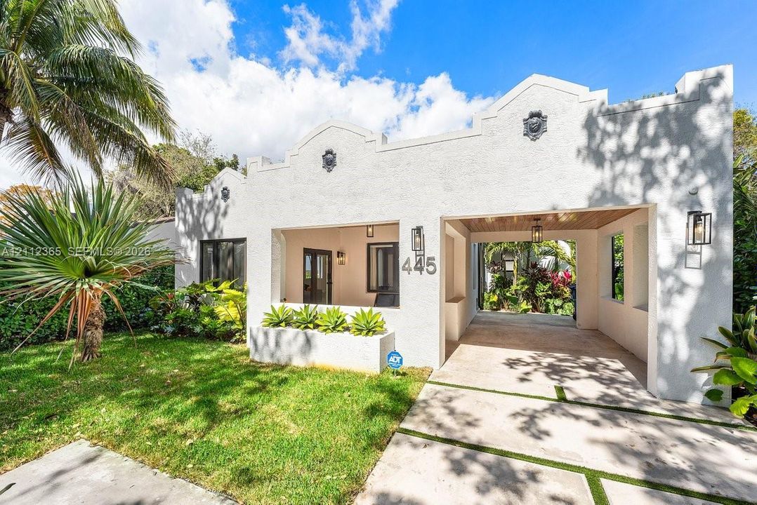 Stucco facade featuring Mission-style roofline detailing, built-in planter box, integrated carport, and exterior wall-mounted lanterns