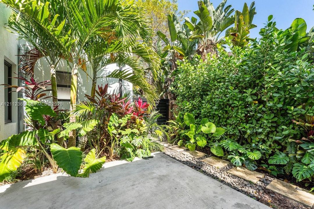 Private outdoor area featuring a concrete patio, stone paver border, river rock accents, and established tropical landscaping